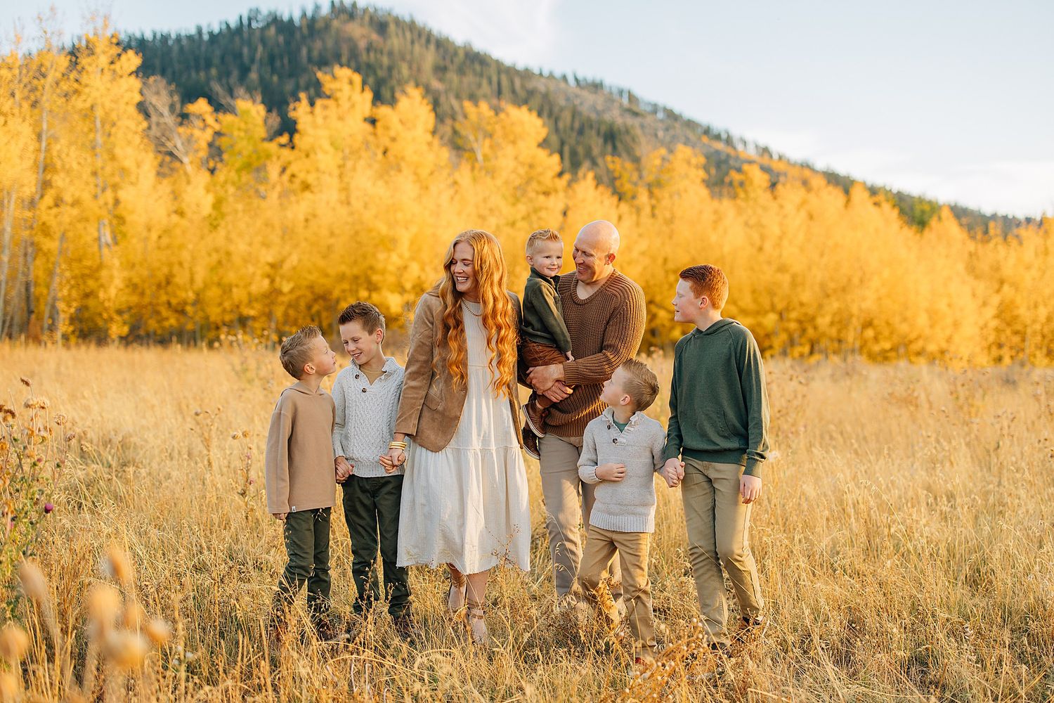 A group enjoying a sunny autumn day in a golden field with mountains in the background.