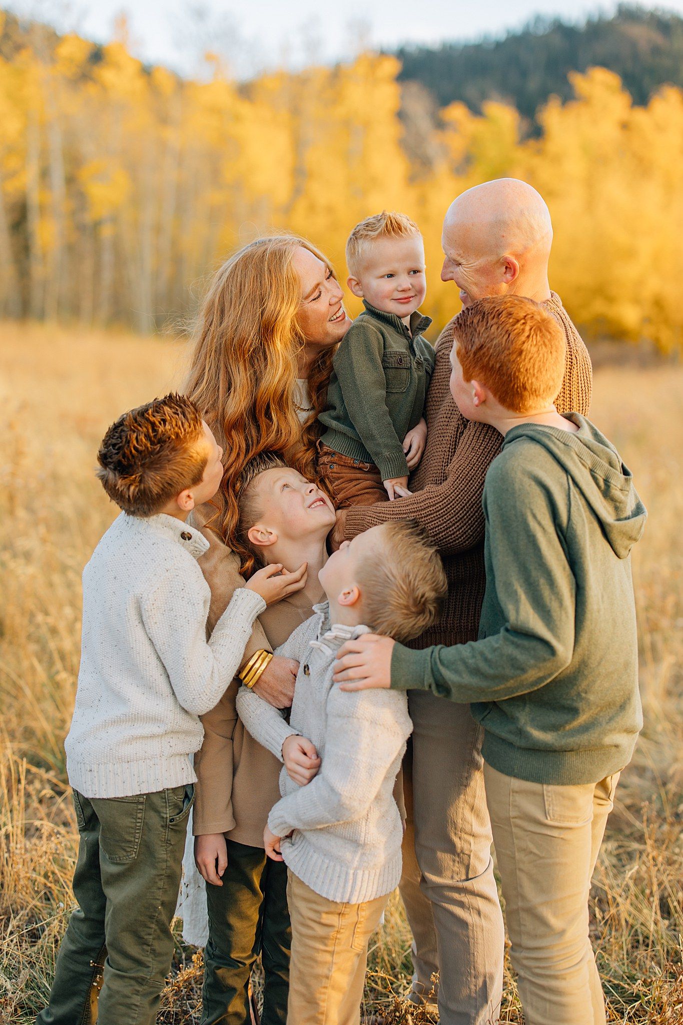 Family shares joyful embraces in a golden autumn field during sunset photo session.