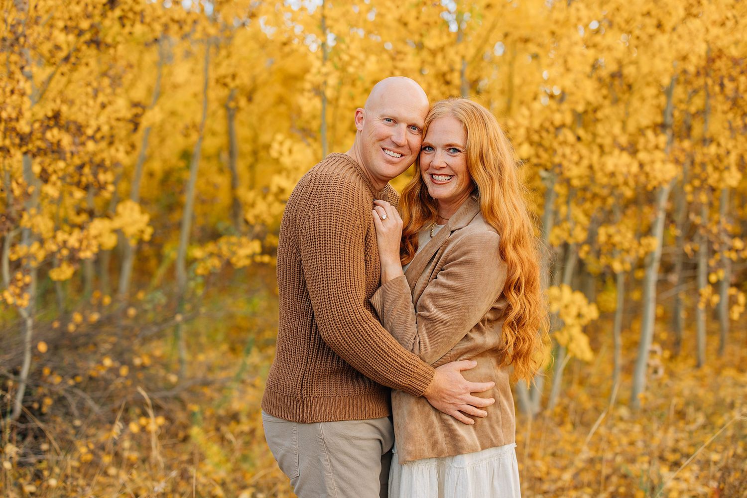 Couple embraces lovingly in autumn forest surrounded by golden yellow aspen trees and falling leaves.