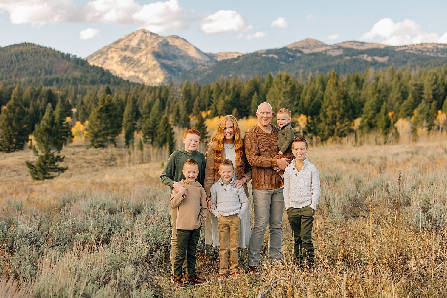 A group stands together in a golden mountain meadow at sunset with evergreen forests and peaks in the background.