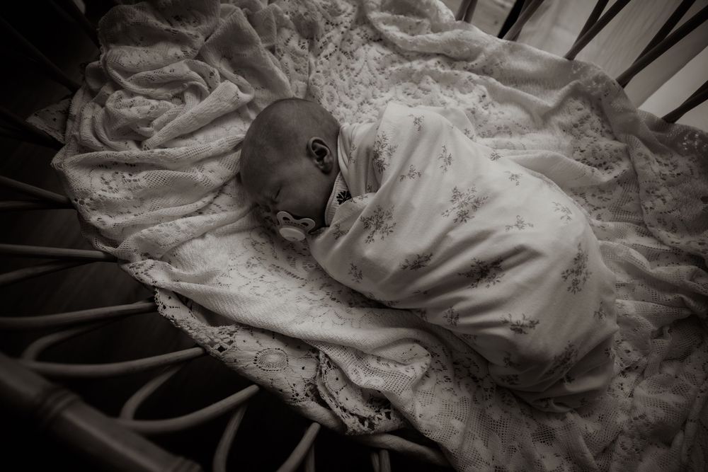 Lifestyle newborn photography in DFW in studio bassinet, baby wrapped gently in blanket