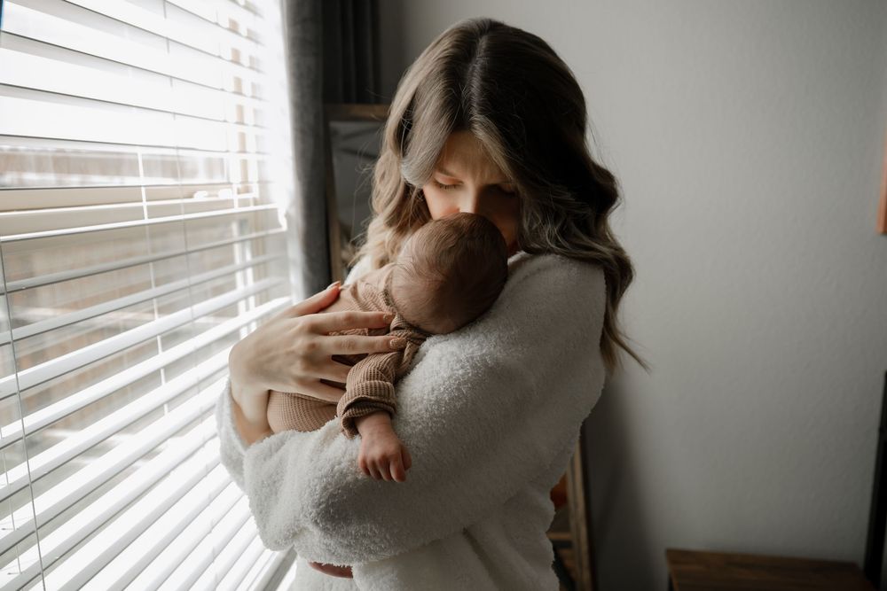 In home lifestyle newborn photography session with mom holding the baby in natural window light