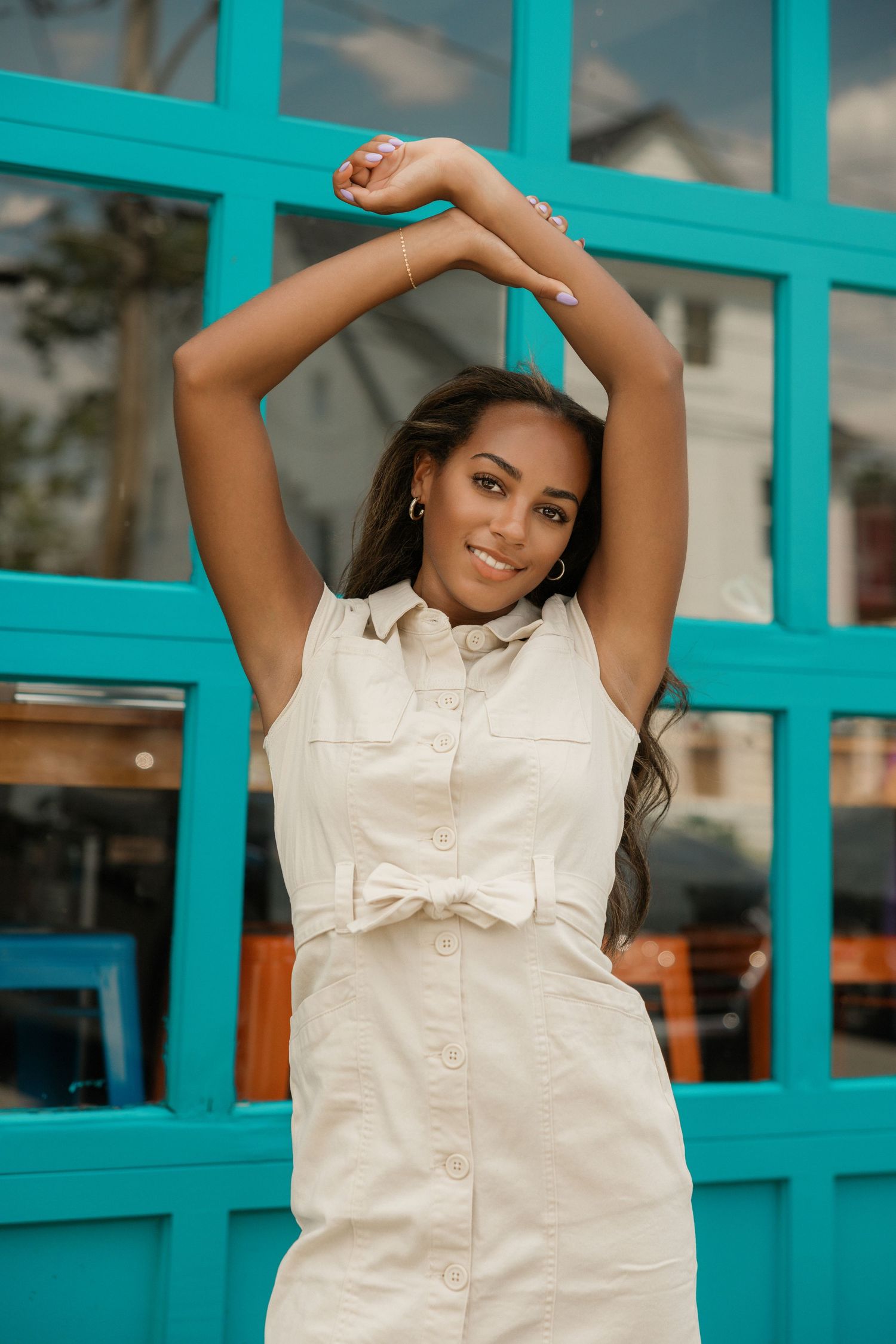 Stylish poses against turquoise storefront wearing white button-down outfit.