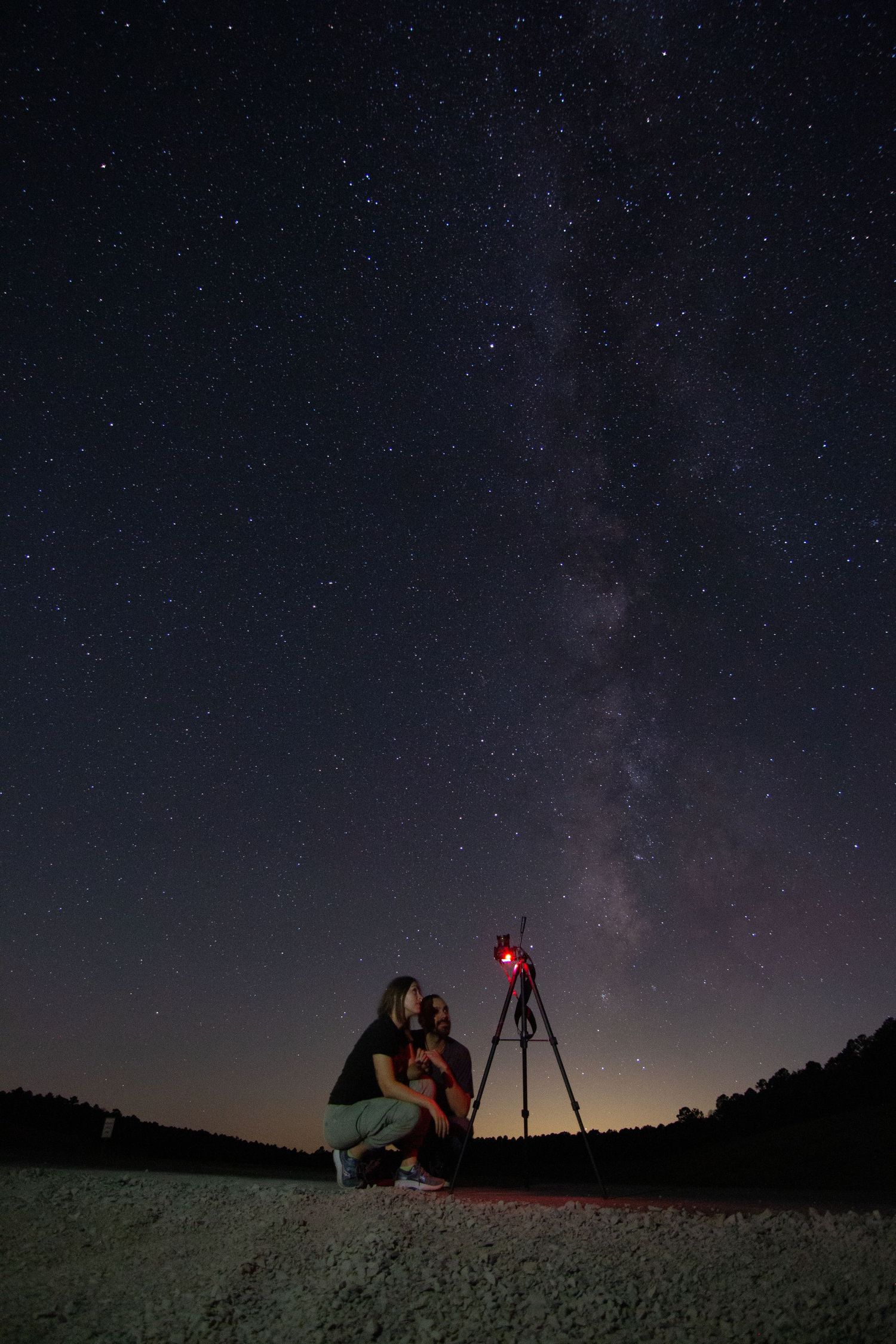 Silhouettes of stargazers with equipment set up under the Milky Way galaxy in a dark night sky.