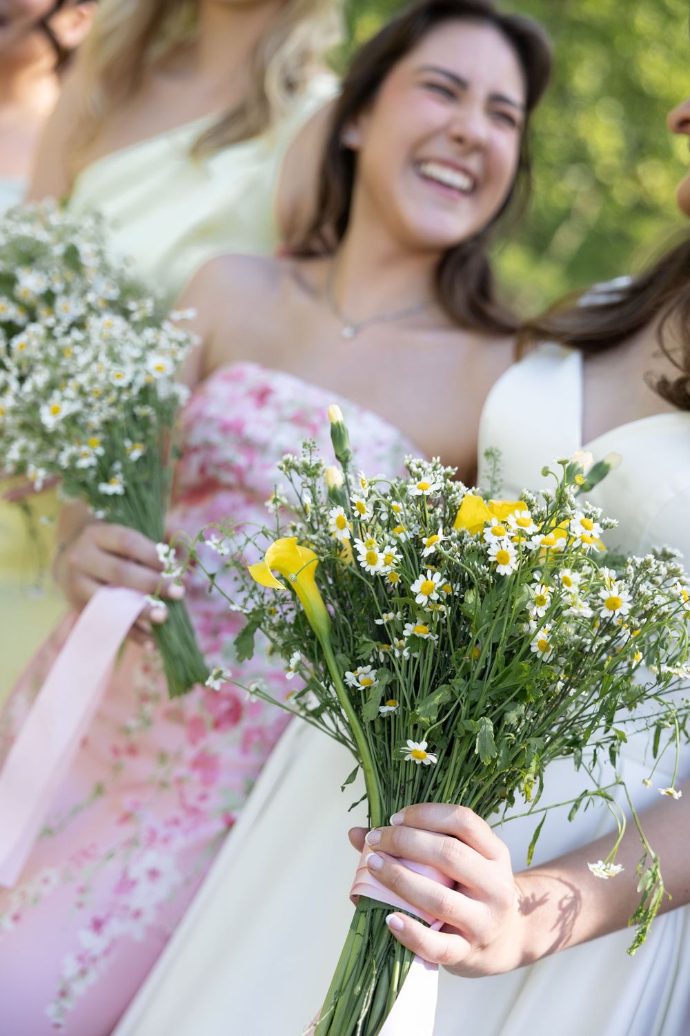 Someone in a pink dress holds a fresh bouquet of white daisies and yellow wildflowers in a sunny outdoor setting.