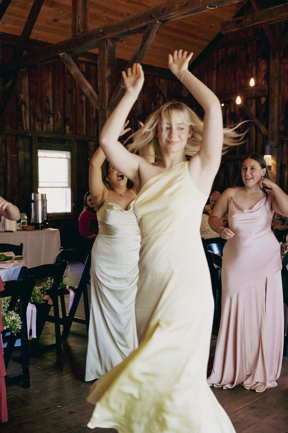 Wedding party guests dancing and celebrating in a rustic wooden barn venue with natural lighting.