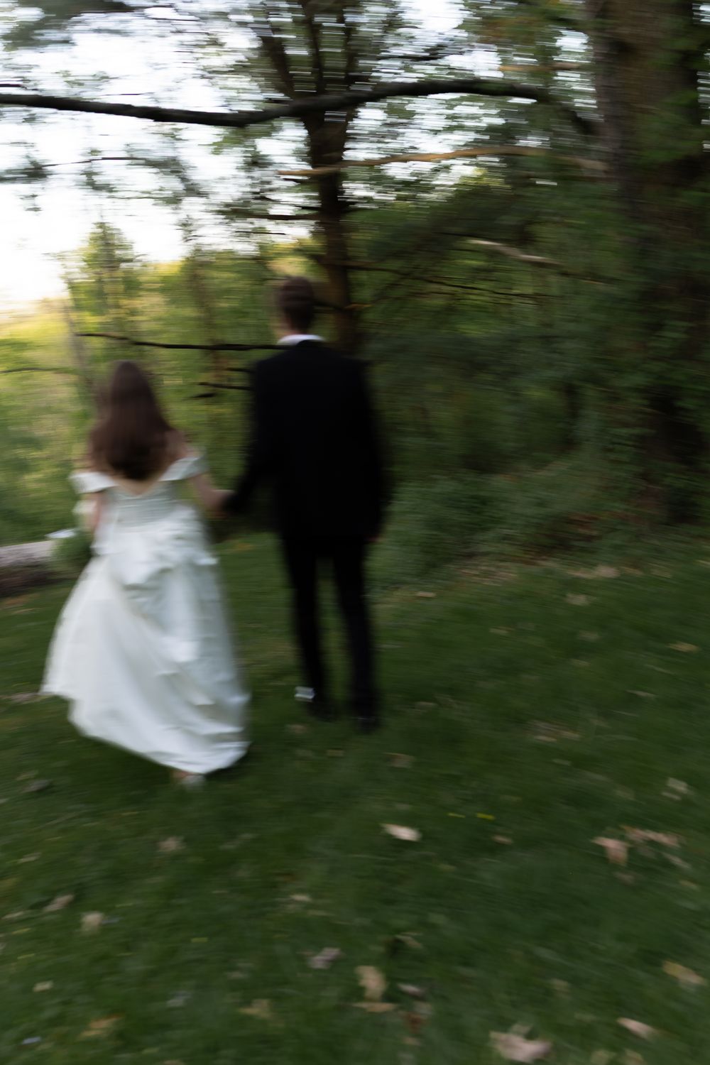 Two figures in formal attire walk together through a wooded area in a series of blurred motion shots.