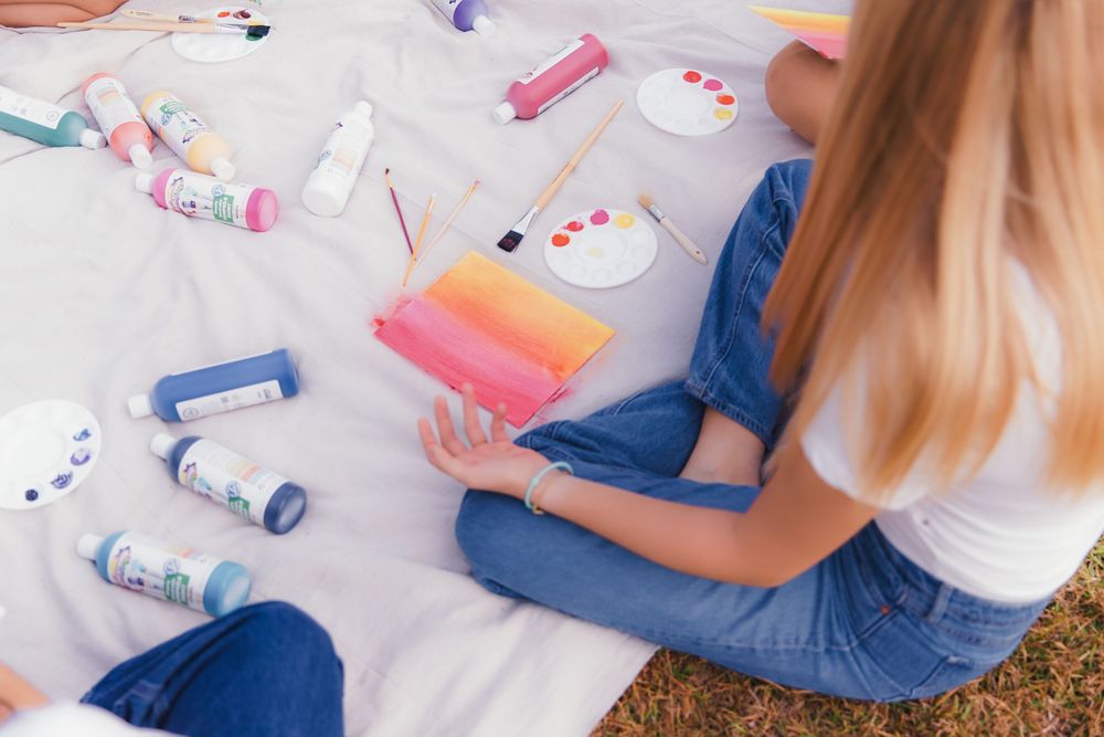 A person sitting on the floor wearing blue jeans and a white shirt while playing with colorful toys and craft supplies.
