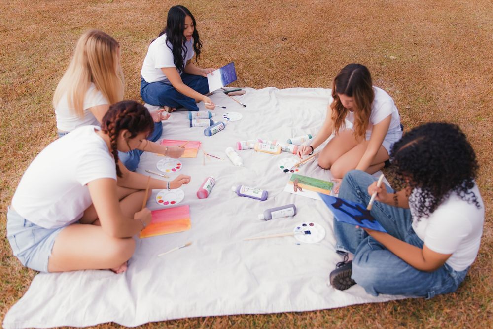 Students sitting on grass collaborating together on a large art project spread out on white paper.