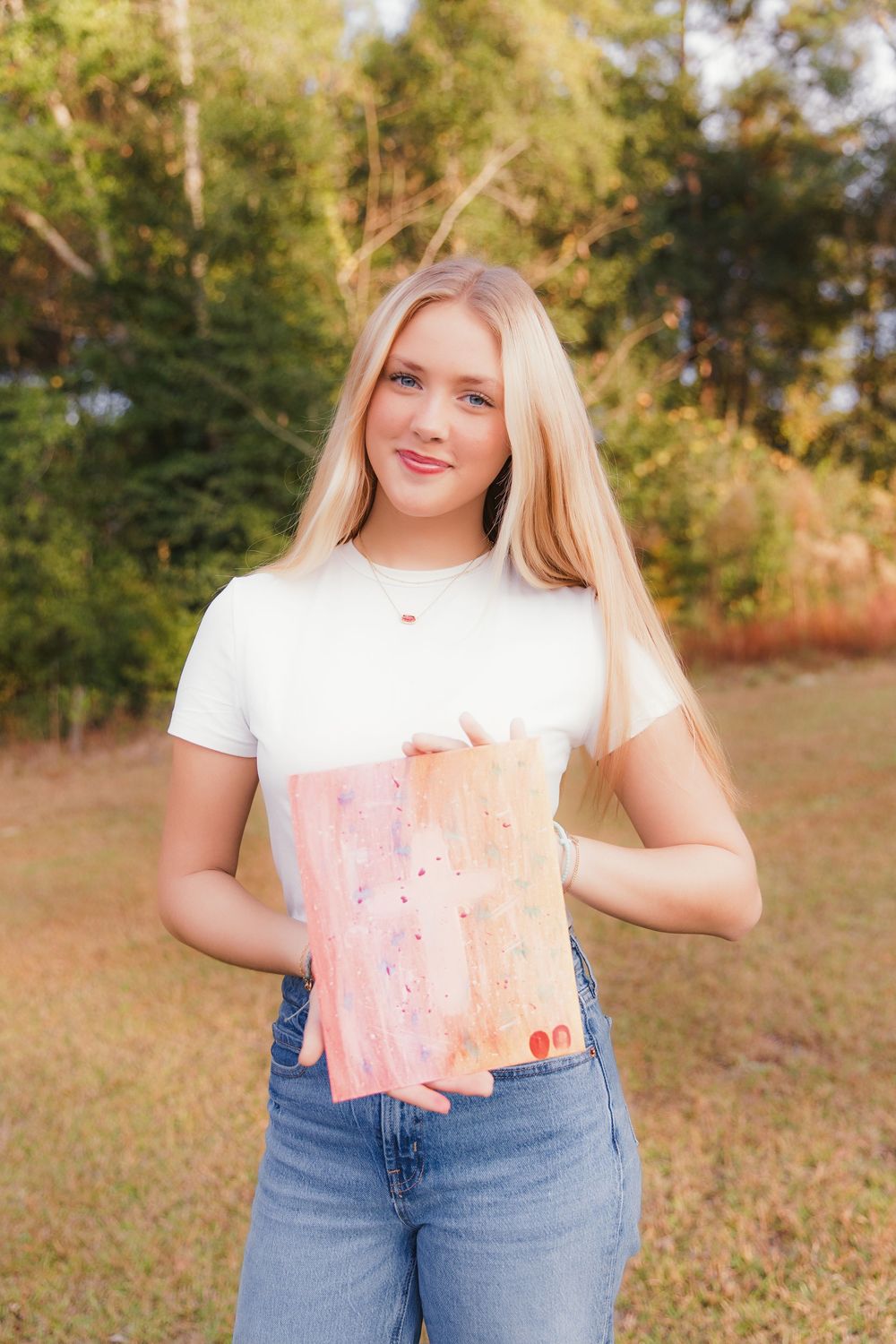 A casual outdoor photoshoot featuring someone in a white t-shirt and jeans against a wooded background.
