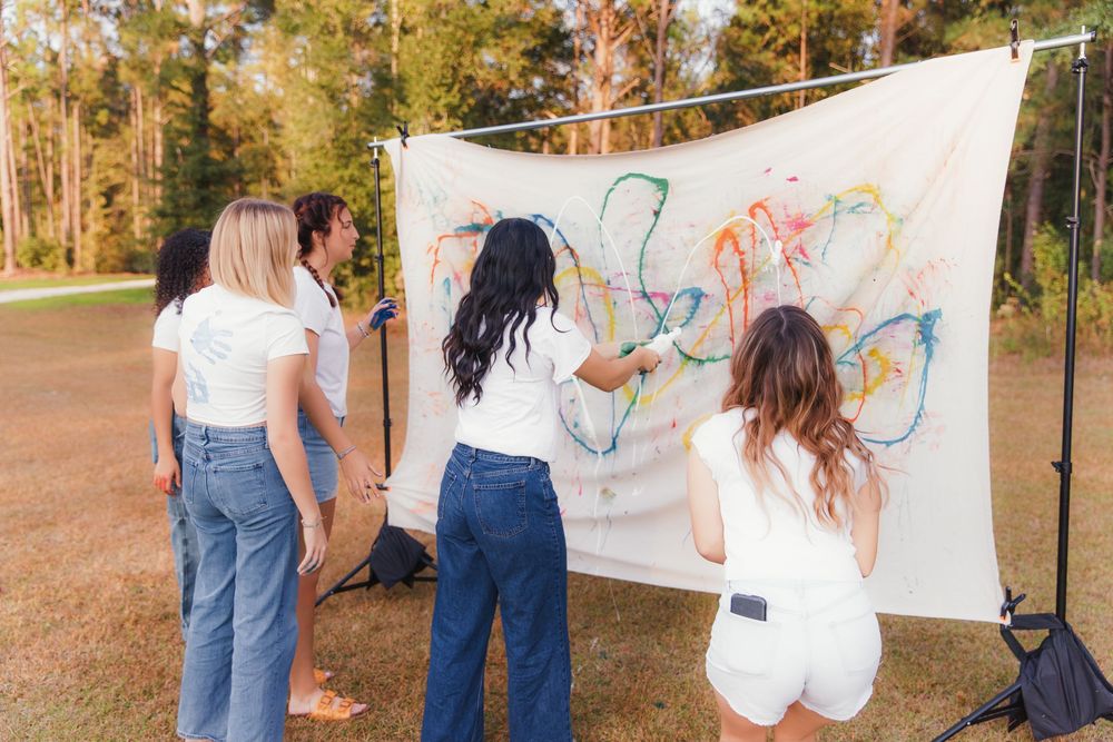 Group of friends in white shirts and jeans work together on a large outdoor art project in autumn setting.