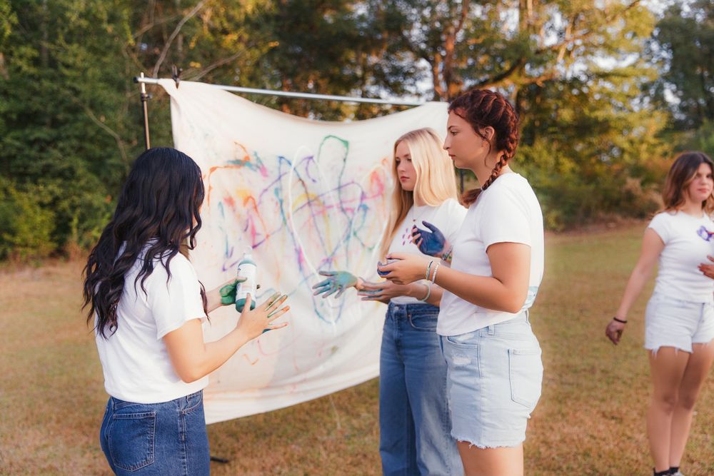 People collaborating on a creative outdoor painting project with white canvas against natural backdrop.
