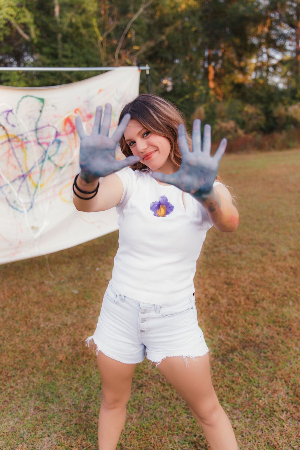 Four sequential photos show someone in white clothing playfully posing with paint-covered hands outdoors in autumn.