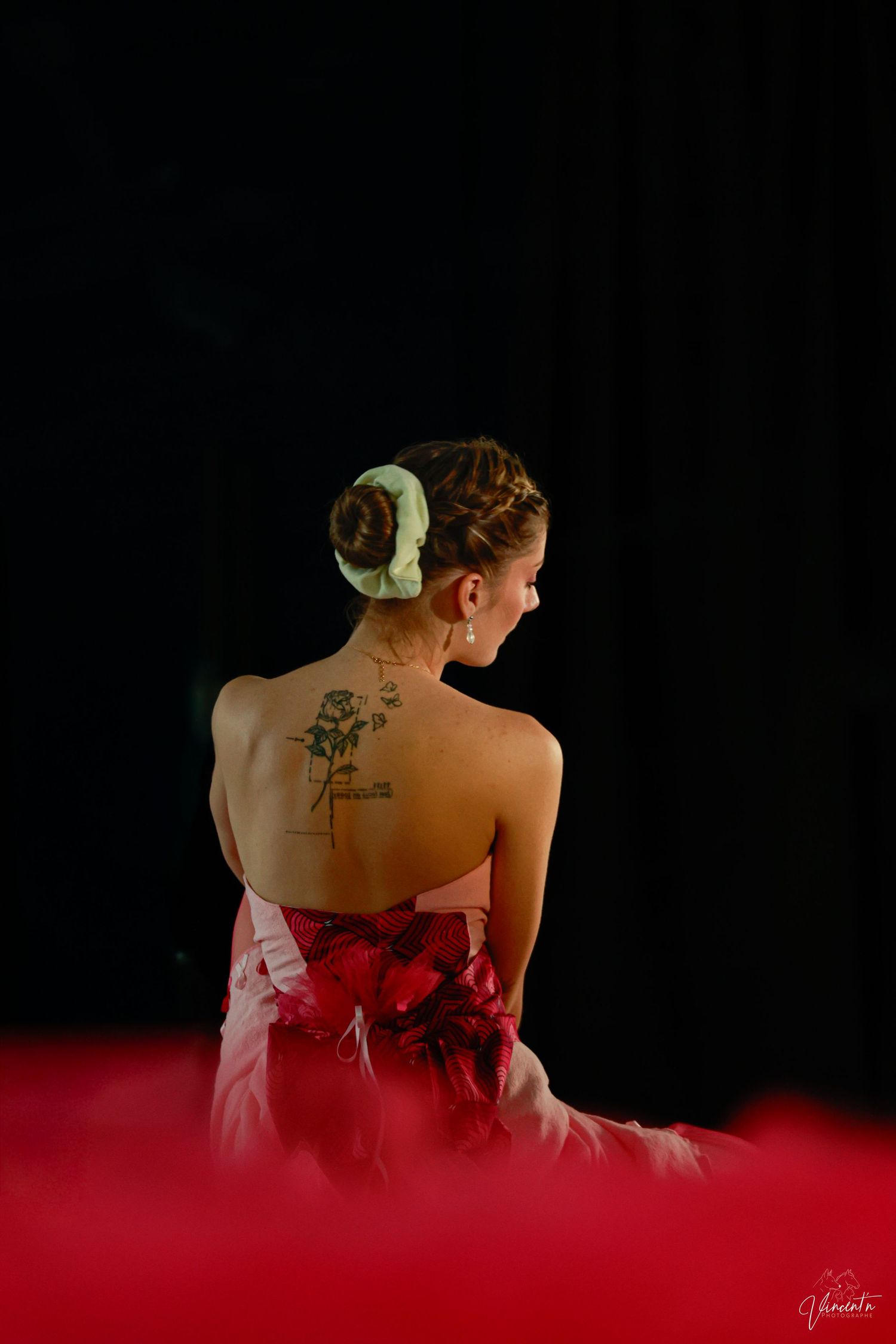 Artistic portrait showing tattoo art on bare back against red and black background.