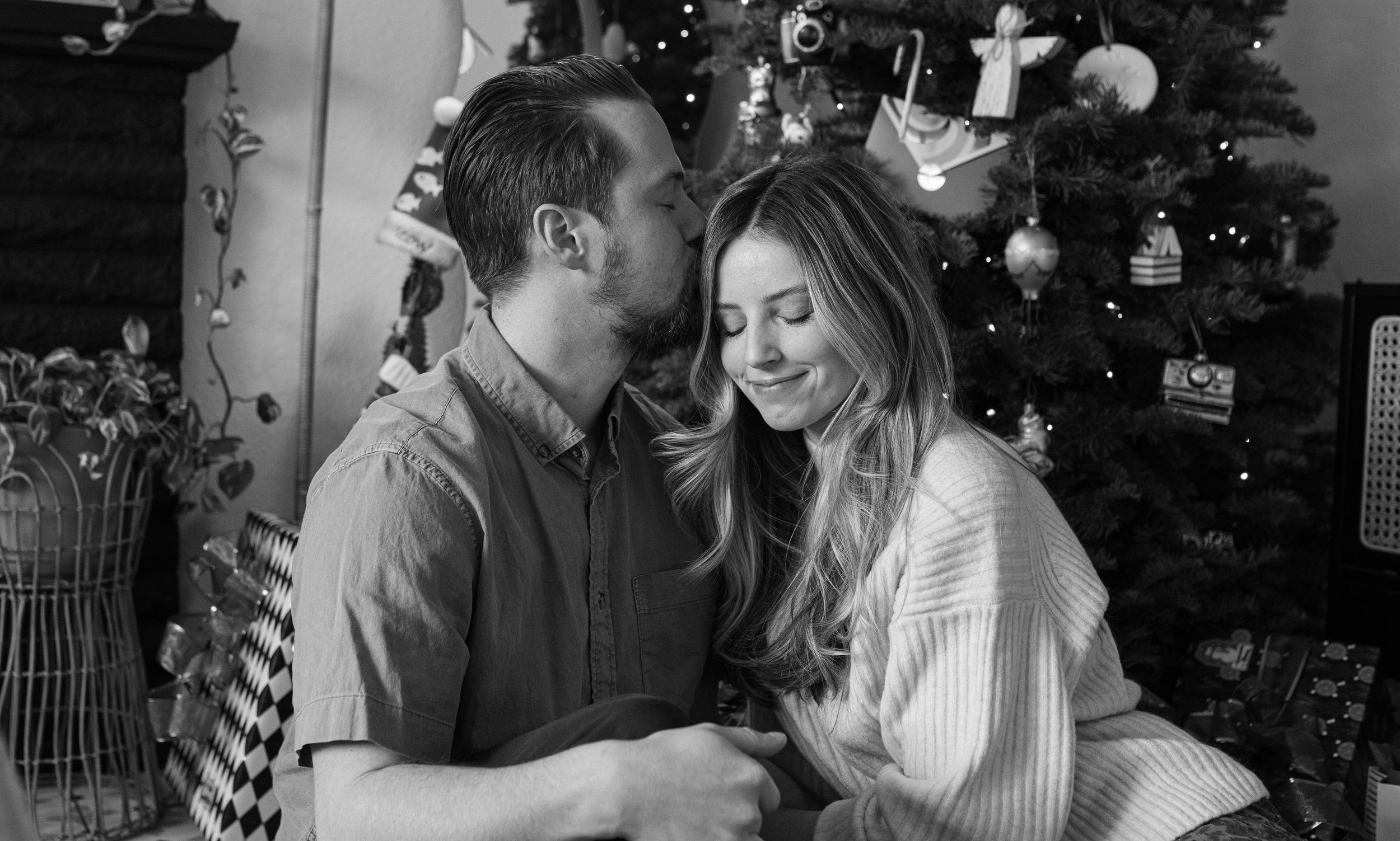 A romantic couple shares tender moments in front of a decorated Christmas tree in a series of black and white photos.