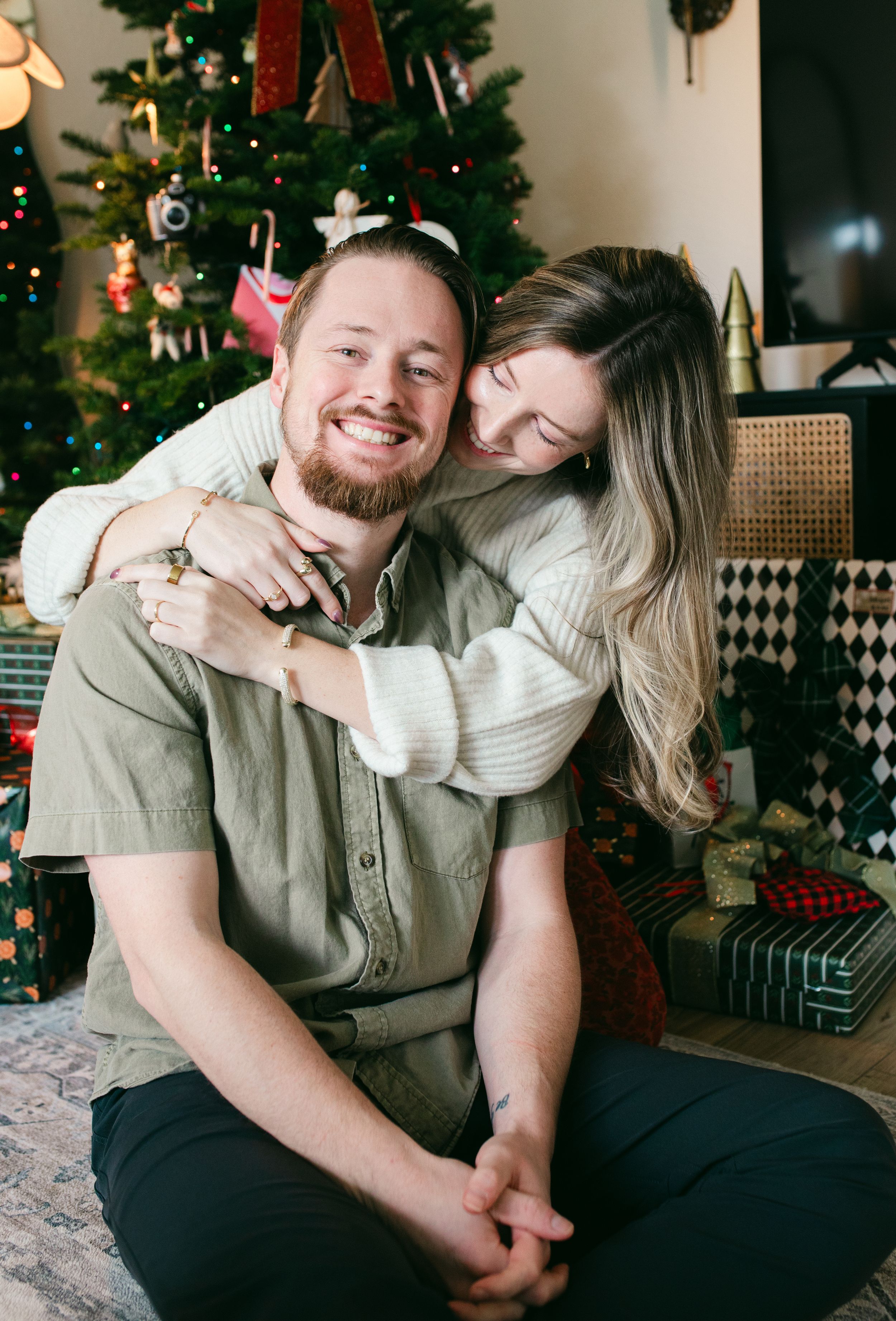 A cozy holiday scene with people sharing affectionate moments on a sofa near a decorated Christmas tree.