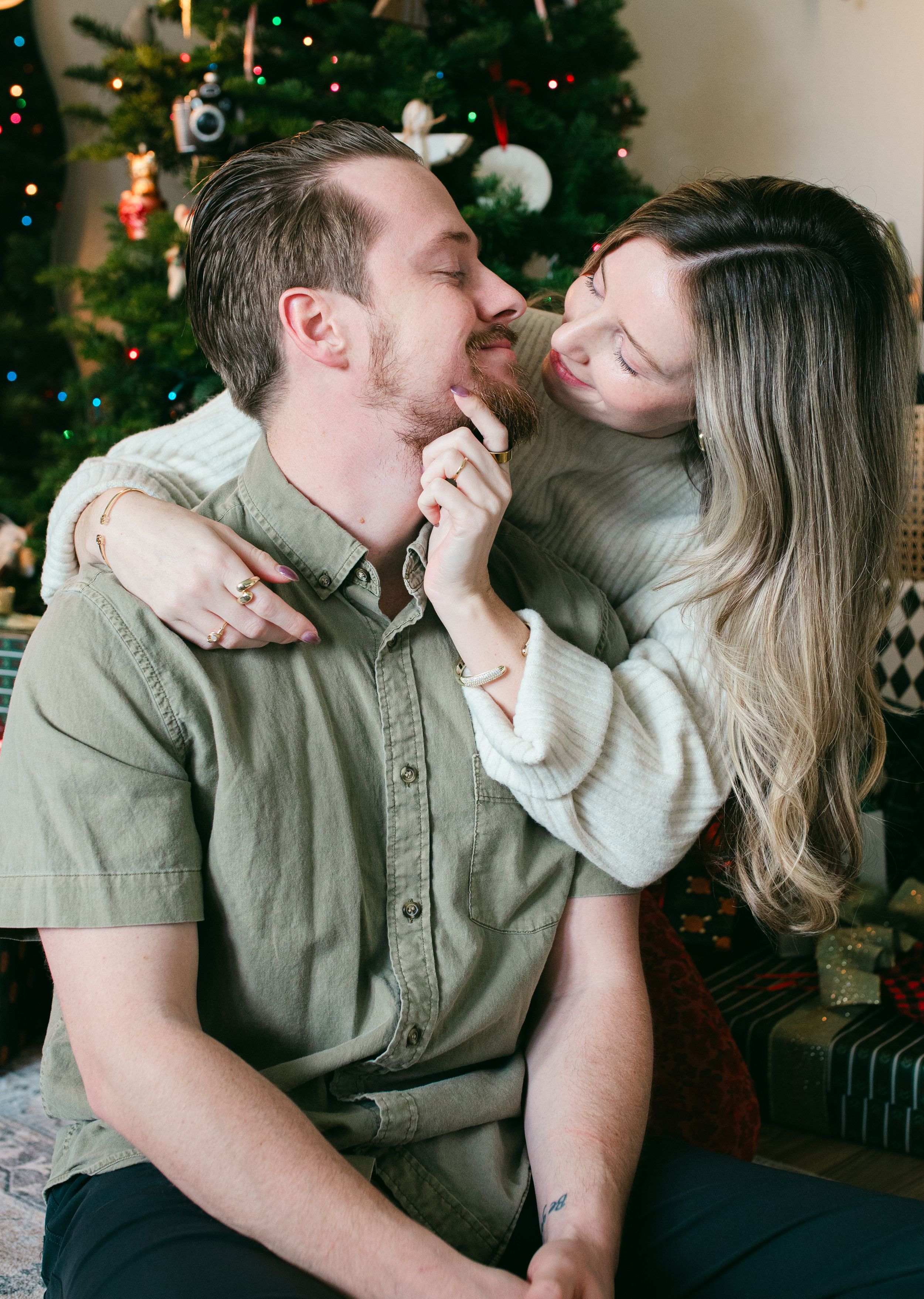 Romantic couple sharing intimate moments in front of a decorated Christmas tree with twinkling lights.