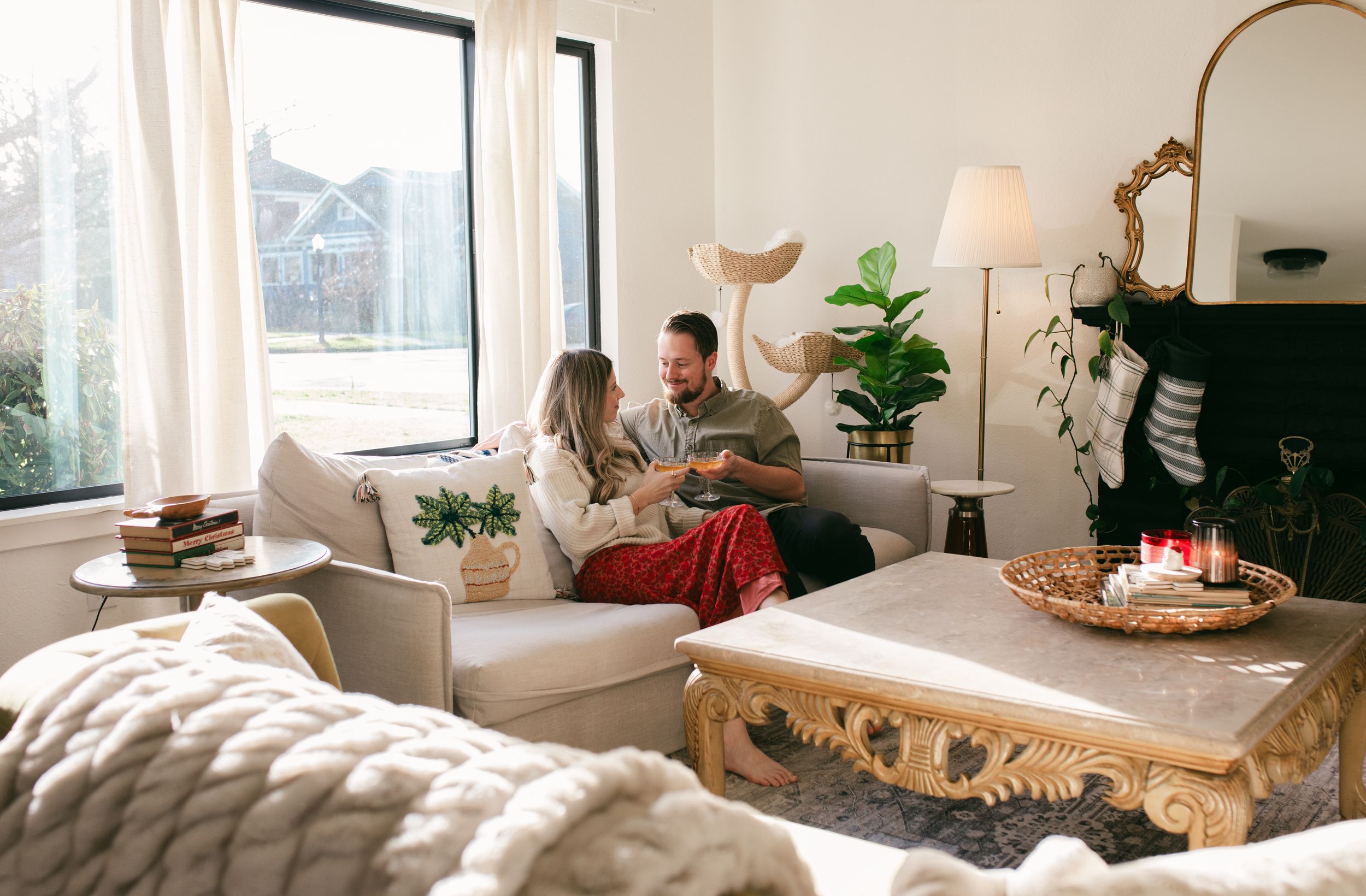 Cozy living room decorated for Christmas with a tree, plants, and natural light streaming through windows.