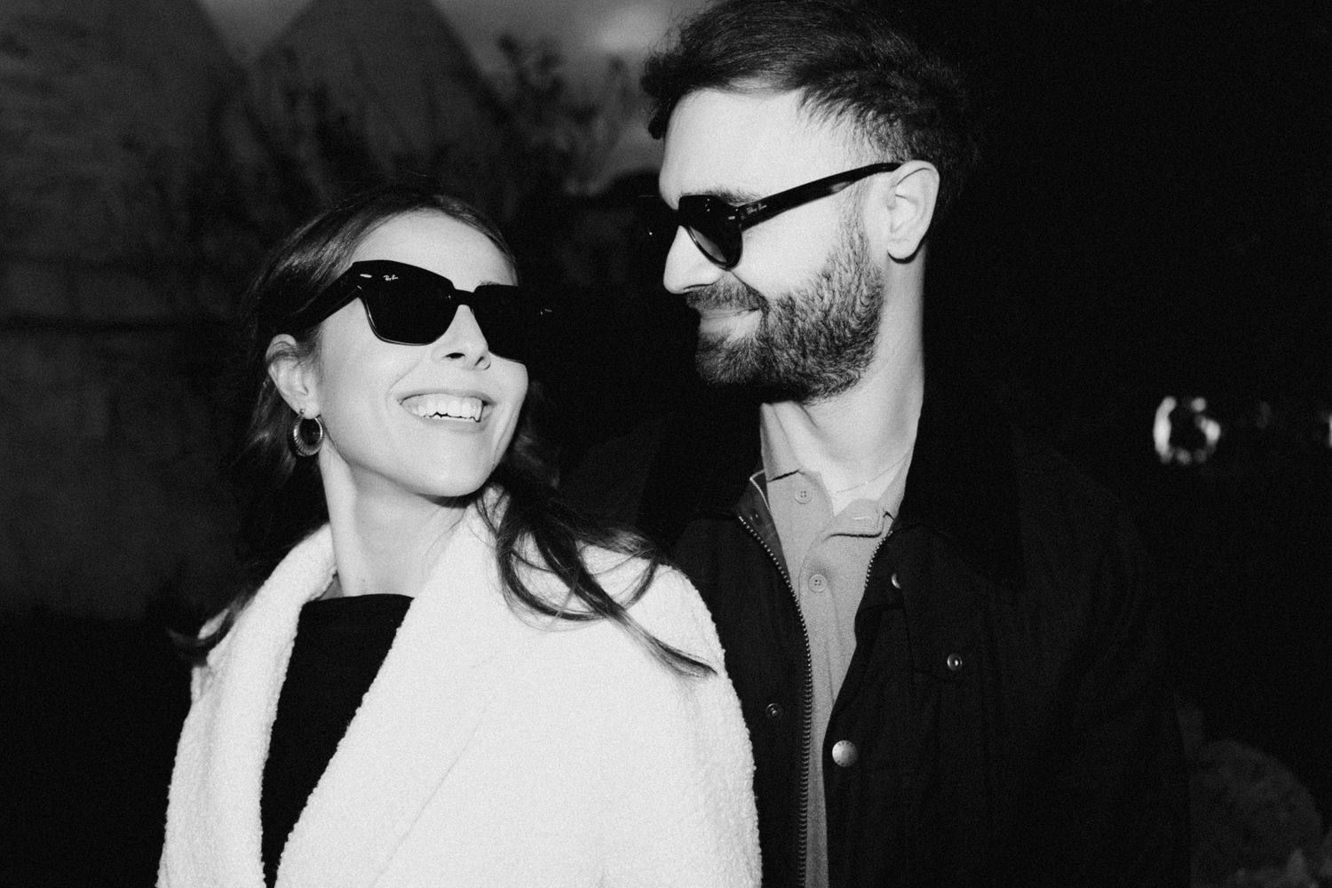 A series of black and white photos showing a couple in sunglasses sharing intimate moments and laughter together.
