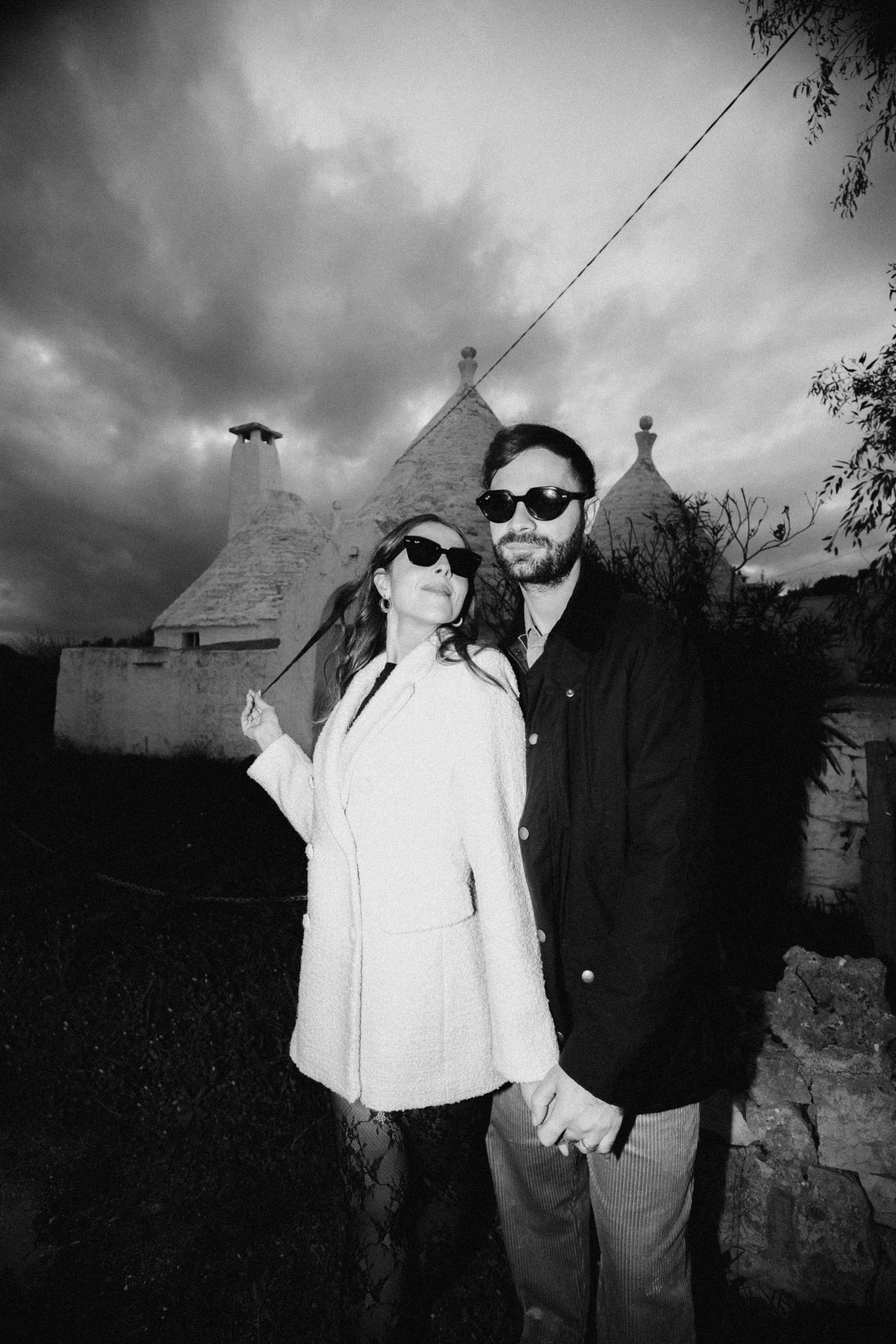 A series of black and white photographs showing two people posing together against a dark cloudy sky and buildings.