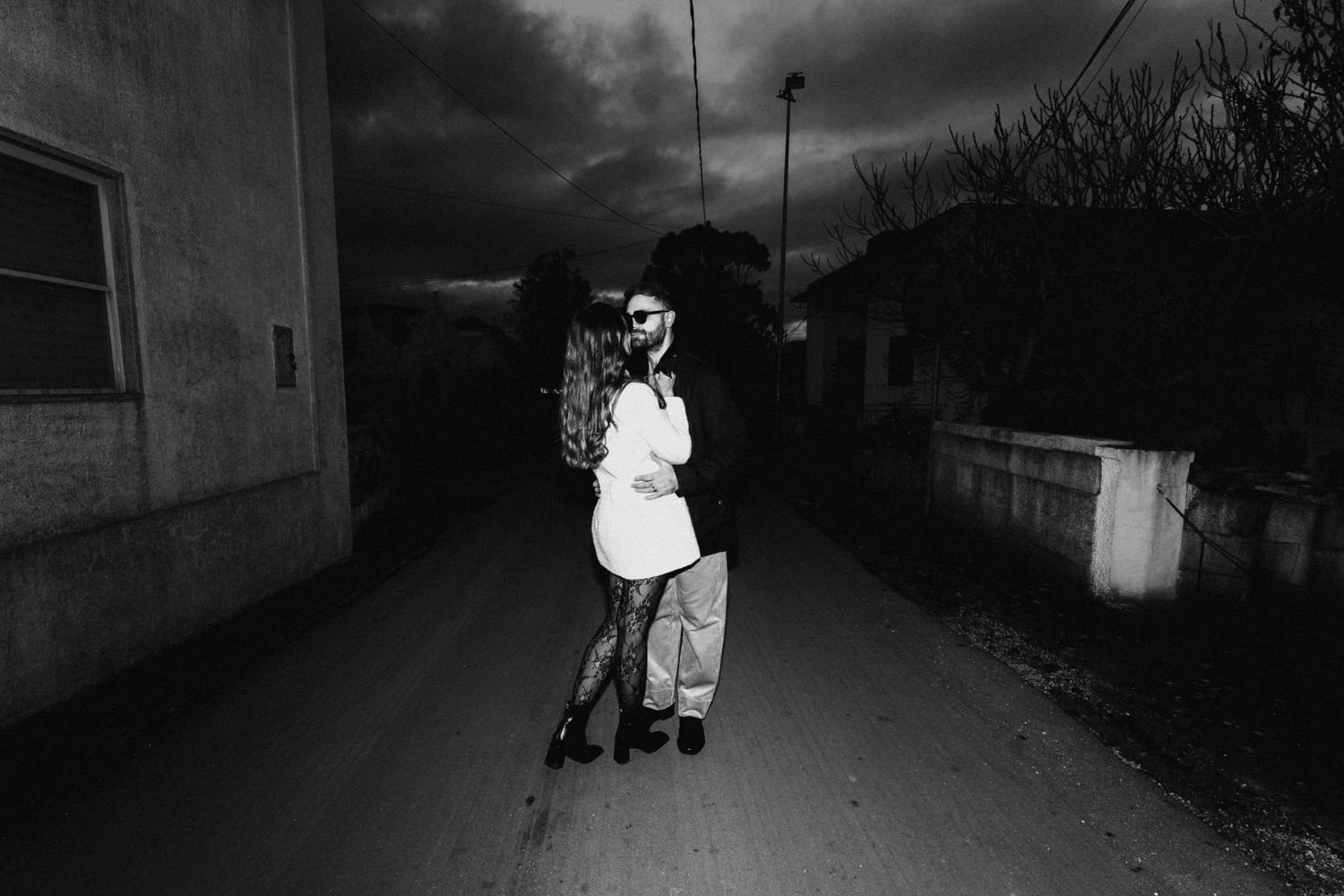 A couple embraces on a dark street at night in black and white photography.
