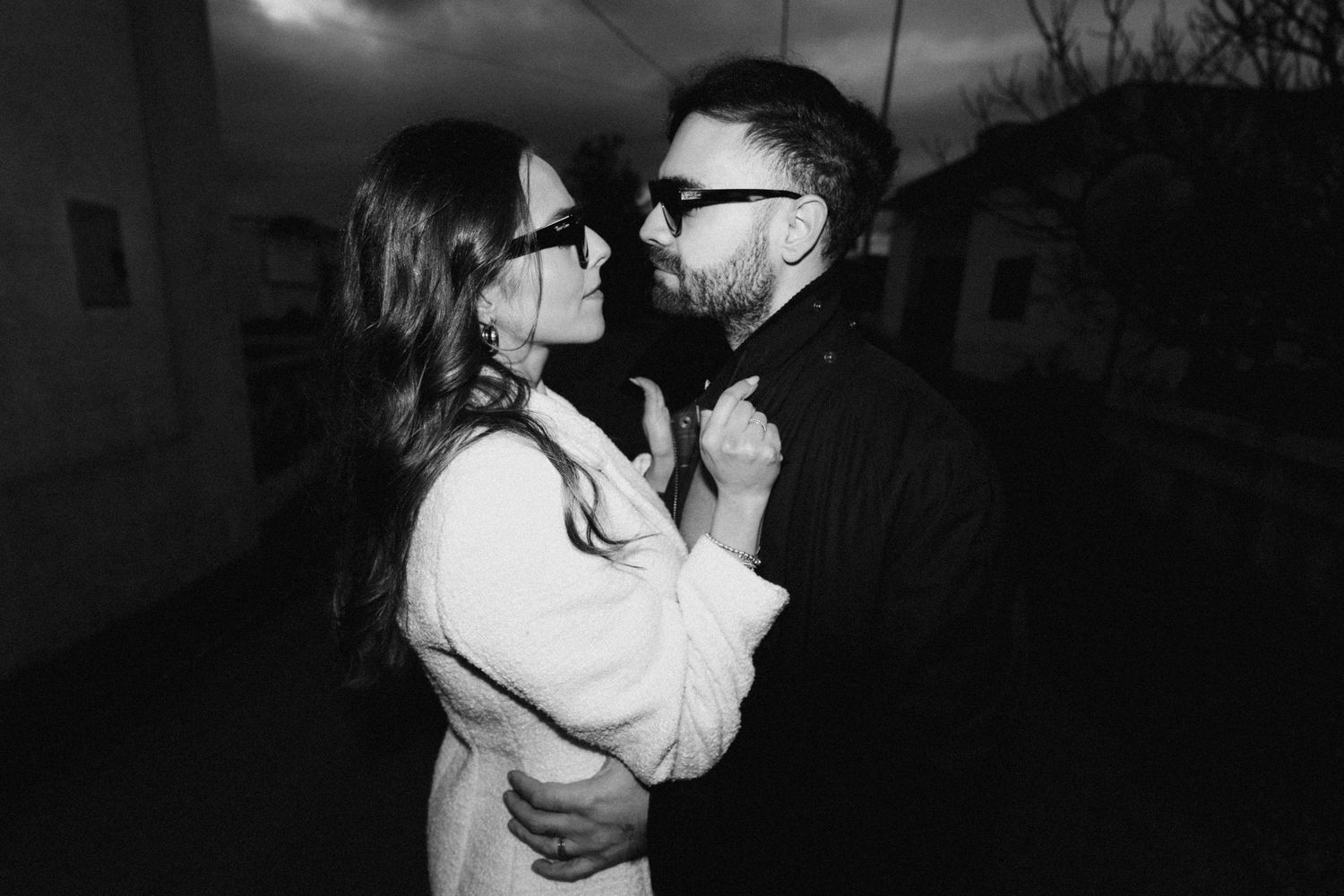A romantic black and white photo of a couple embracing outdoors at dusk.