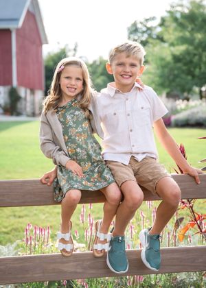 Children sit together on a wooden fence wearing coordinated outfits on a sunny afternoon.