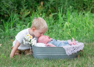 A young child lies on grass near a galvanized metal tub in a garden setting.