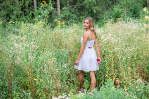 Young person in a white dress walks through a lush green meadow filled with wildflowers on a sunny summer day.