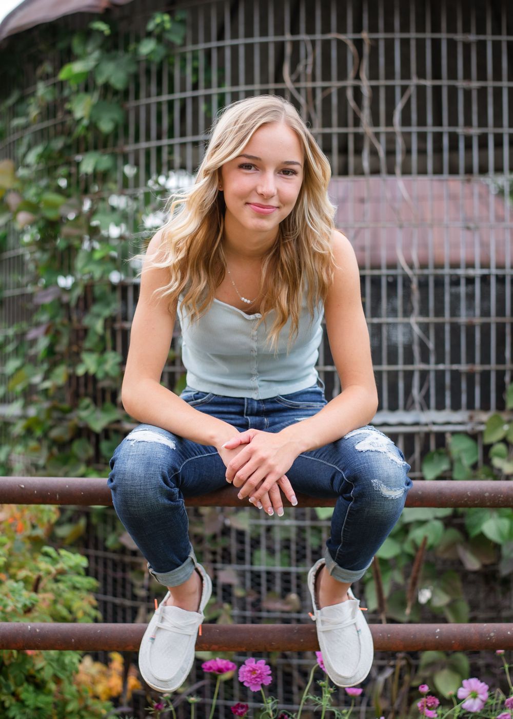 A casual portrait on a metal railing with greenery and flowers in the background.