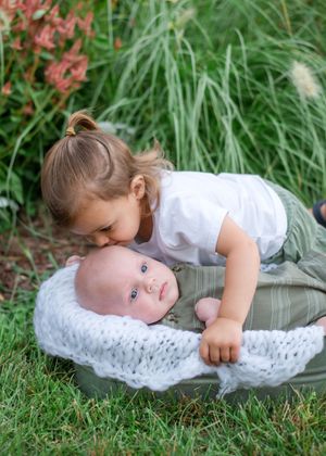 A child lies peacefully on a white lace blanket in the grass during an outdoor photo session.