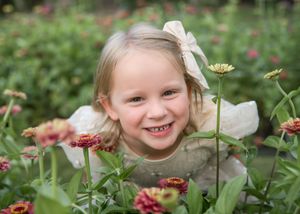 A young child peeks through blooming flowers in a lush garden setting.