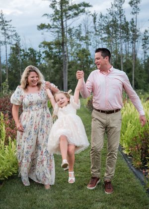 A family shares joyful moments together while swinging and playing in a grassy field surrounded by pine trees.