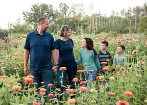 A family stands together in a vibrant field of colorful wildflowers and tall grass on a sunny summer day.
