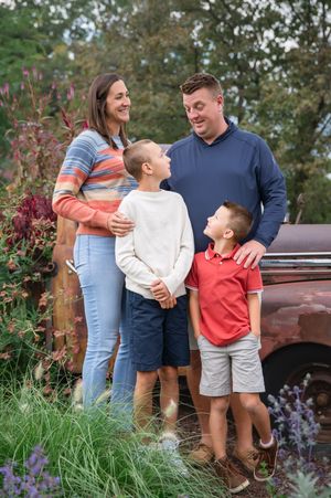 A casual outdoor family photo session featuring a vintage pickup truck and flowering garden backdrop.