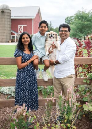 A family poses with their small dog in front of a red barn and silo on a sunny summer day.