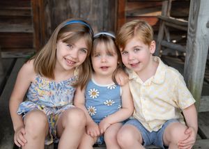 Four children sitting together on wooden steps wearing coordinating blue and cream colored outfits.