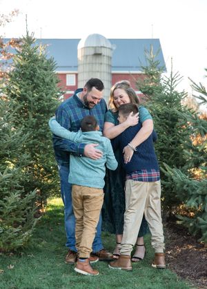 Family playfully interacts while shopping for Christmas trees at an outdoor tree lot.