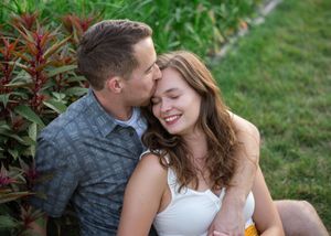 A couple shares a tender moment outdoors in a garden setting with green foliage in the background.