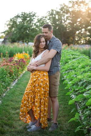 A couple embraces in a lush garden filled with vibrant flowers and greenery during golden hour.