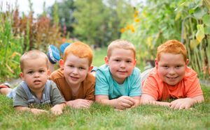 A row of children lying in green grass and wildflowers on a sunny summer day.