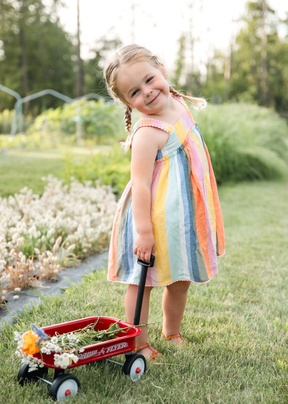 A colorful striped dress and red wagon create a playful summer scene in a grassy backyard.