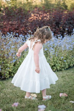 Little girl in white dress twirls and dances in a garden with blooming flowers in the background.