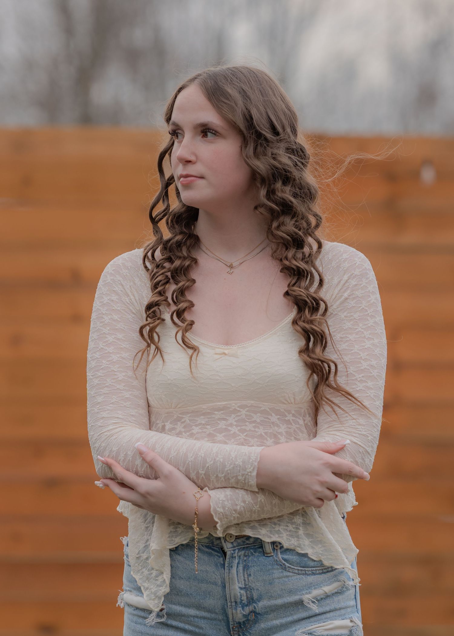 Person in cream sweater and distressed jeans poses against wooden wall.