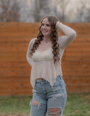 Casual pose in ripped jeans and textured cream sweater outdoors.