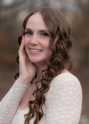 Portrait showing curled hair and cream lace sweater against natural background.
