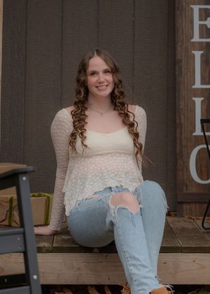 Casual sitting pose on wooden deck wearing cream sweater and light denim.