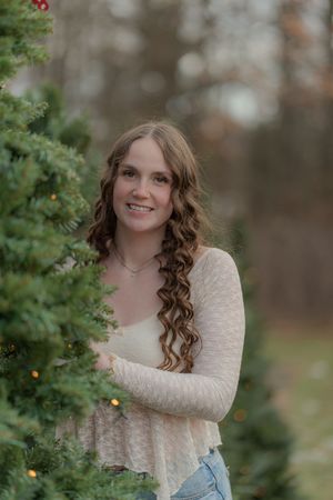 Outdoor winter photoshoot among evergreen trees with twinkling lights.