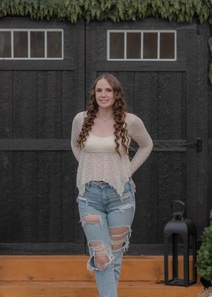 Portrait against dark wooden wall wearing distressed jeans and cream sweater.
