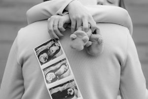 A couple in light colored clothing holds ultrasound photos during a photo session.